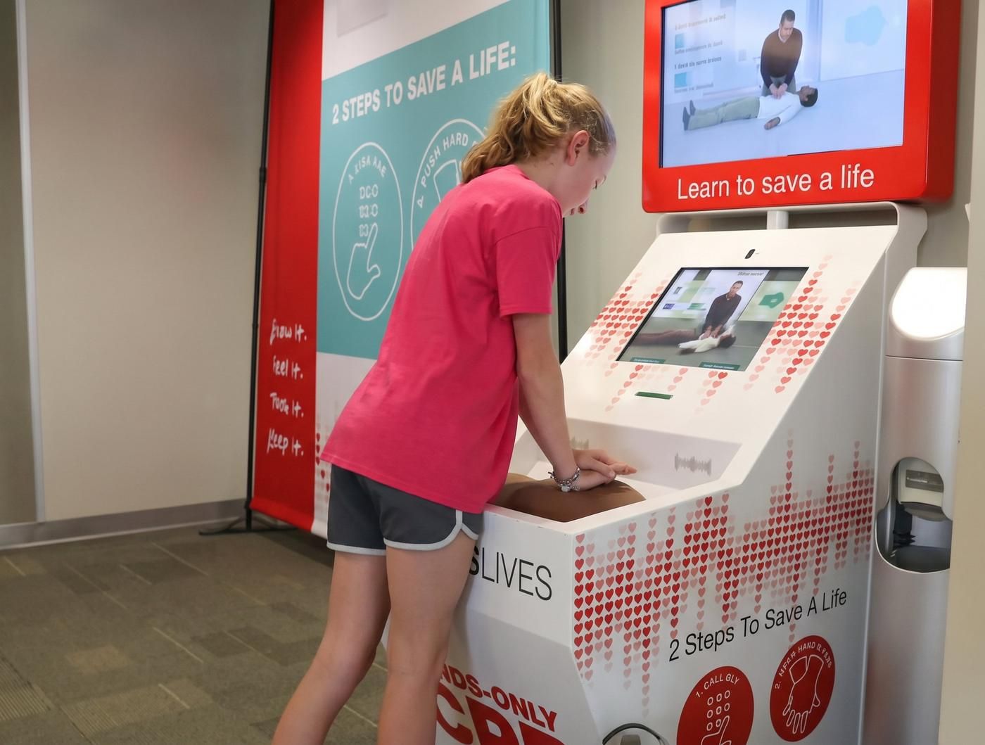 A girl practices hands-only CPR on a CPR training kiosk with real-time feedback